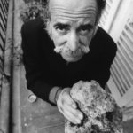 William Saroyan standing on his balcony holding a piece of rock from Armenia.