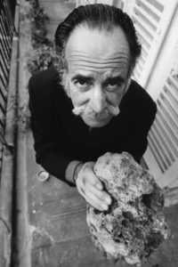 William Saroyan standing on his balcony holding a piece of rock from Armenia.
